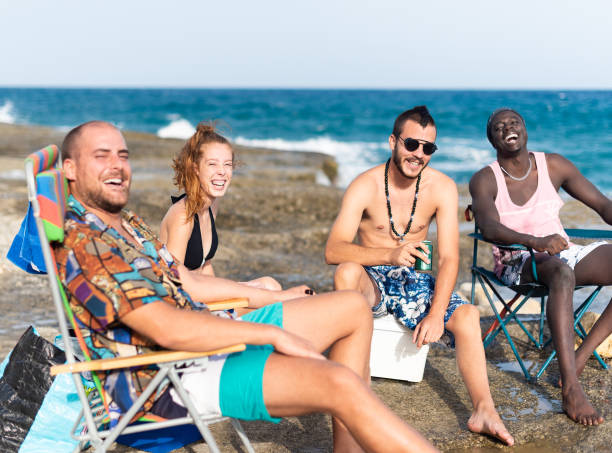 quatre jeunes prenant un bain de soleil sur une plage rocheuse - shirtless beach women bikini photos et images de collection