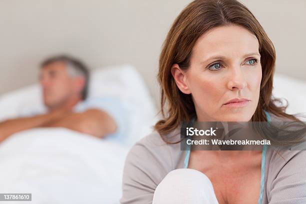 Sad Woman On Bed With Her Husband In The Background Stock Photo - Download Image Now