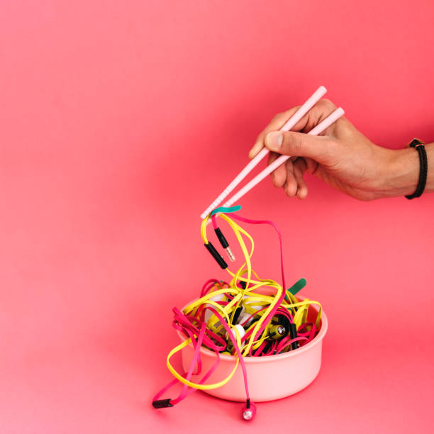 hand with chopsticks holding earphones over pink background stock photo