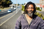 Homeless man with beard and dreadlocks outdoors in city in sunny weather