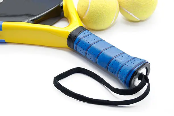 Blue handle of a yellow and black paddel racket with two tennis balls