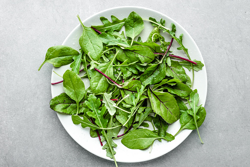 Fresh green salad mix with spinach, arugula and beet leaves on plate, top view
