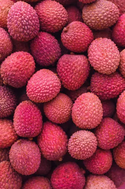 Photo of many ripe red unpeeled lychees - vertical food background