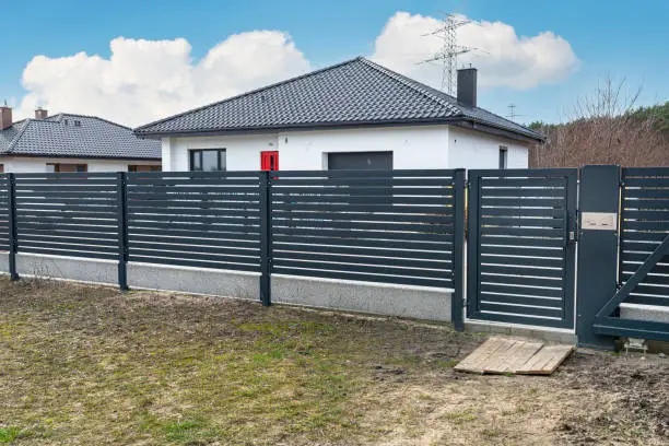Modern panel fencing in anthracite color, visible spans and a gate with a letterbox, view from the garden.