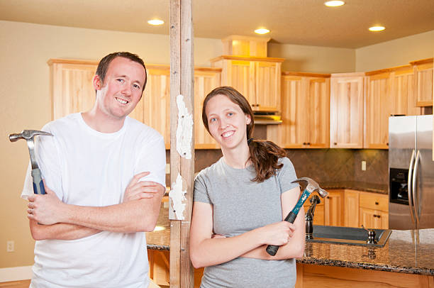 Couple posing for photo in a kitchen holding hammers  stock photo