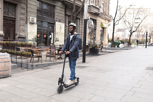 Portrait of the African American young man riding an electric push scooter through the city