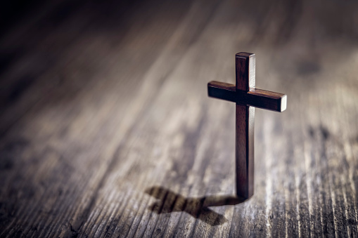 Cruz de crucifijo religioso en posición vertical sobre fondo de mesa de madera photo