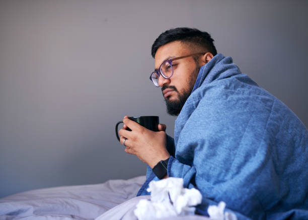 istock A sick man sits in bed wrapped in a blanket holding a warm drink. Copy space 1378895101