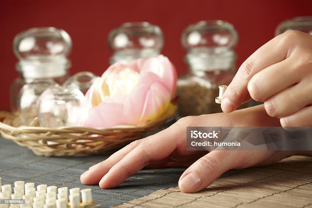 Mini moxa stick therapy TCM Traditional Chinese Medicine. Hand applying mini moxa stick therapy, natural herbs in glass jars in background Acupuncture Stock Photo