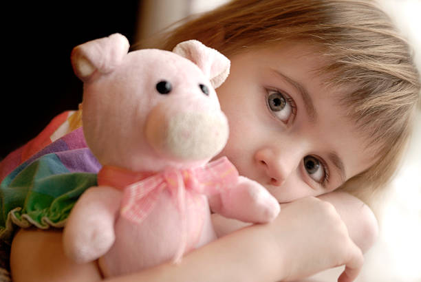 Little girl holding her stuffed animal pig by window light