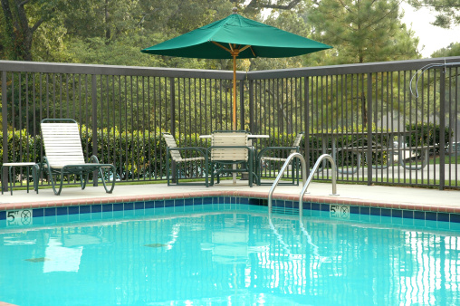 Peaceful poolside scene, with umbrella, table, and chairs.