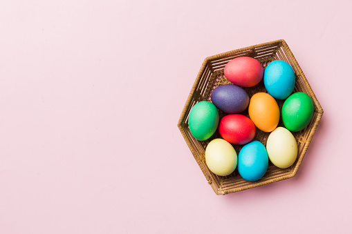 Multi colors Easter eggs in the woven basket on colored background . Pastel color Easter eggs. holiday concept with copy space.