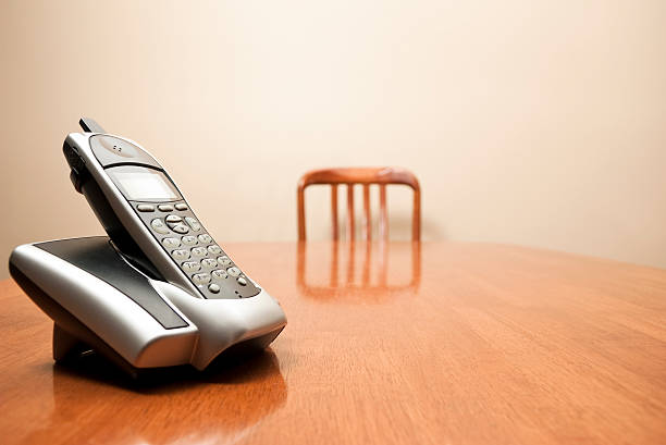 Modern cordless phone sitting on a table A modern cordless phone sits on an empty table. Focus on phone in foreground. More in this series: house phone stock pictures, royalty-free photos & images