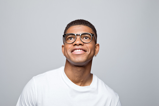 Happy african young man wearing white t-shirt and eyeglasses, looking up and laughing. Studio portrait on grey background.