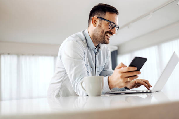 istock A smiling businessman using phone and typing on the laptop at home. 1379022495