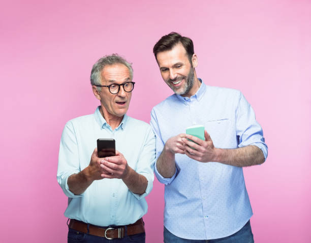 homem feliz compartilhando telefone inteligente com o pai sênior - mid adult men smart casual white happiness - fotografias e filmes do acervo