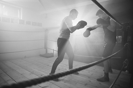 Young man at boxing training, he is sparring and practicing with his coach in boxing ring.