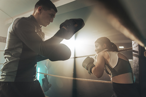 Young woman at boxing training, she is sparring and practicing with her coach in boxing ring.