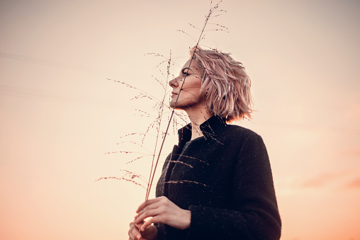Beautiful young woman portrait holding branches in Winter countryside and looking up during sunset
