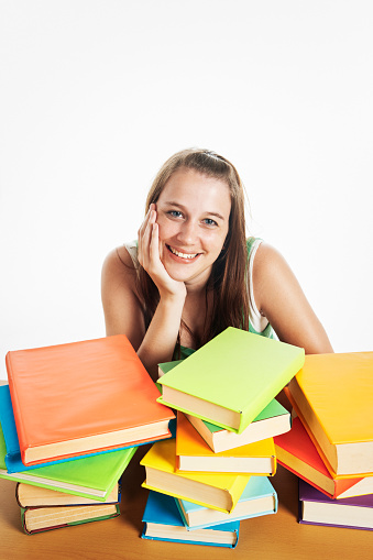 Happy young woman smiles cheerfully as she sits at a desk loaded with books.