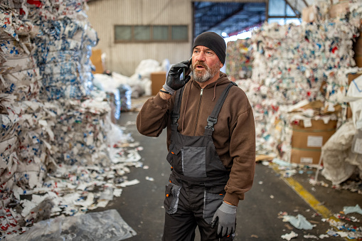 Senior male Caucasian worker,talking on mobile phone while working at the recycling center