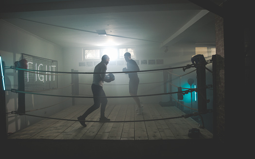 Ringside Black Boxing gloves hanging from ropes in a boxing ring with red boxing pads in a boxing gym no people, Cape Town, South Africa