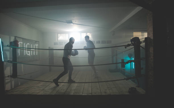 Coach training young boxer Young man at boxing training, he is sparring and practicing with his coach in boxing ring in dark gym. mixed martial arts photos stock pictures, royalty-free photos & images