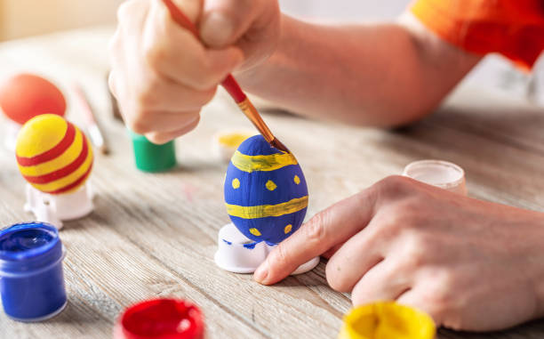 istock Woman's hand with a brush is drawing a colored pattern on an Easter egg. Preparation for the bright Easter holiday 1379157929