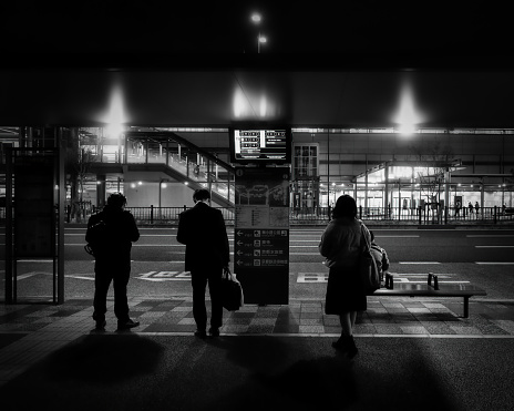 Kyoto, Kyoto Prefecture, Japan - November 25, 2021: A small group of people wait at a bus stop in front of the main train station.