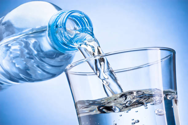 wasser aus plastikflasche in glas auf blauem hintergrund isoliert gegossen - gurgling stock-fotos und bilder