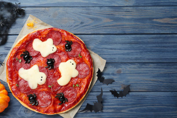 istock Cute Halloween pizza with ghosts and spiders served on blue wooden table, flat lay. Space for text 1379192060