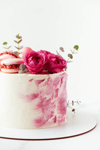 Beautiful birthday cake with pink cream cheese frosting decorated with macaroons and roses. Happy Valentine's day. Anniversary cake on the white background