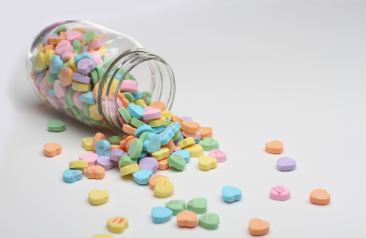 A jar containing colorful candy hearts has tipped over and spilt them