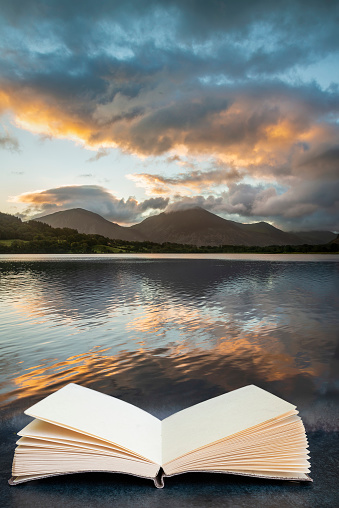 Digital composite image of Stunning sunrise landscape image looking across Loweswater in the Lake District towards Low Fell and Grasmere coming out of pages in reading book