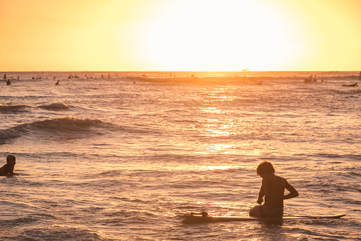 Oahu, USA - Nov 6, 2021: Surfers and Swimmers off Waikiki Queens Beach as the sun sets.