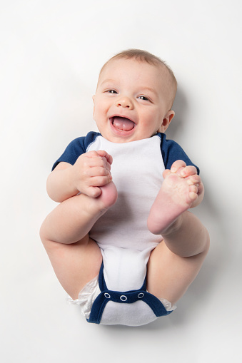 A 6 month old baby boy laughing as he grabs his bare feet.