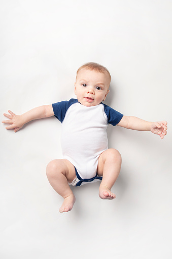 A 6 month old baby boy isolated on white wearing a onesie.
