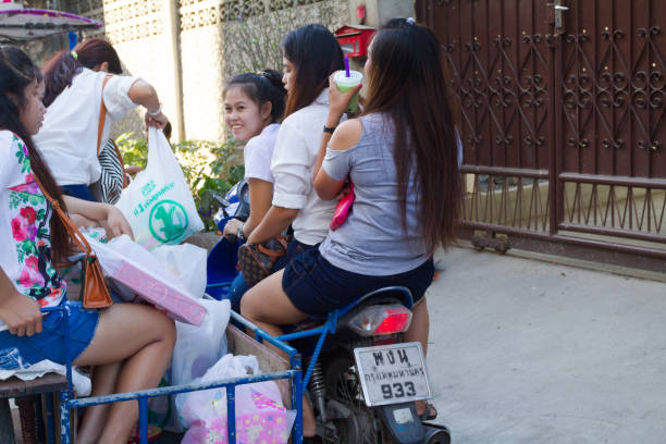 Group of cheerful young thai women is sitting on a motorcycle with side carrier. Women are talking and laughing. Scene is in street near CRU university in Bangkok Chatuchak
