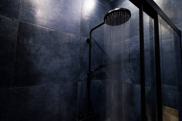 Water running from a black rain shower head in a dark luxury bathroom