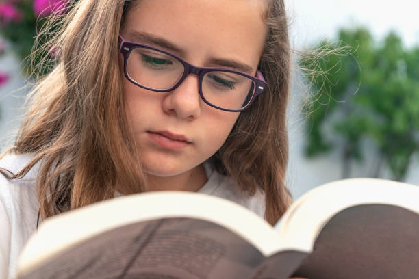 zbliżenie dziewczyny w okularach czytającej książkę na świeżym powietrzu. - adolescence teenagers only teenager making a face zdjęcia i obrazy z banku zdjęć