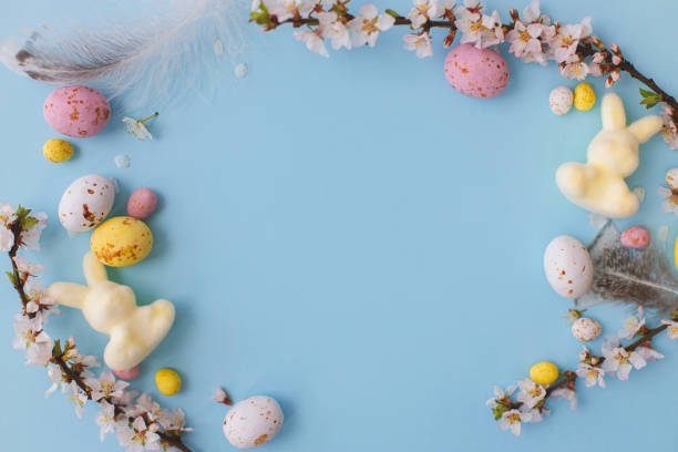 istock Colorful Easter chocolate eggs, bunny, cherry blossoms border on blue background. Happy Easter!  Easter flat lay with space for text. Greeting card or banner. Stylish tender spring template 1379295438