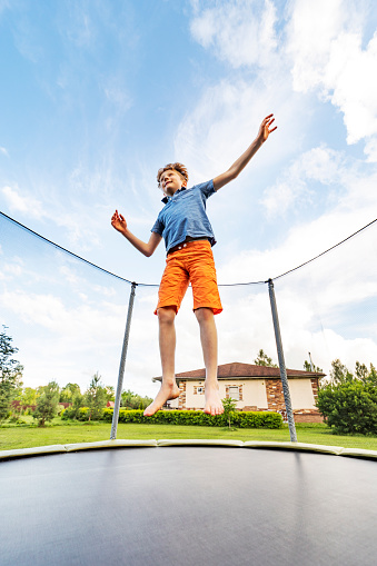 Little preschool girl jumping on trampoline. Happy funny toddler child having fun with outdoor activity in summer. Sports and exercises for children. Trampolin in ukrainian flagg colors.