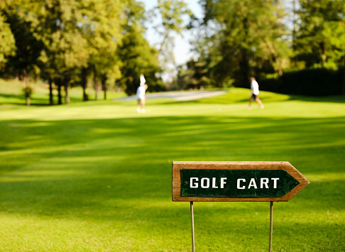 Sign near the green indicating the prohibition of driving by golf car. In the background the green with the players.