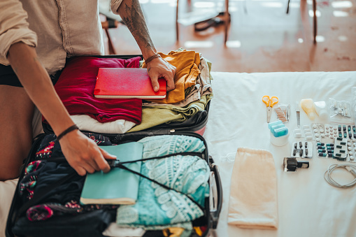 An unrecognizable man packs clothes and all the necessities for traveling in a suitcase.