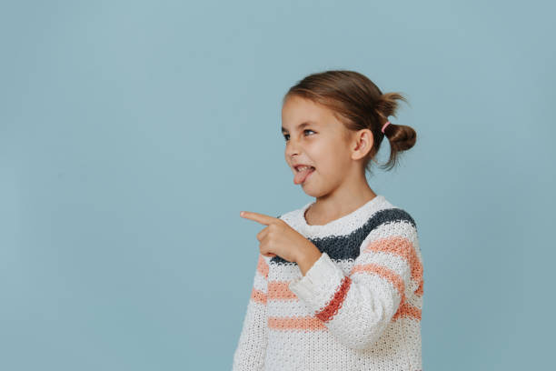 Teasing nasty little girl points her finger and sticks out tongue over blue stock photo
