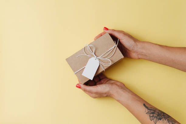istock Female hands placing cardboard box with a tag on a yellow surface 1379318106