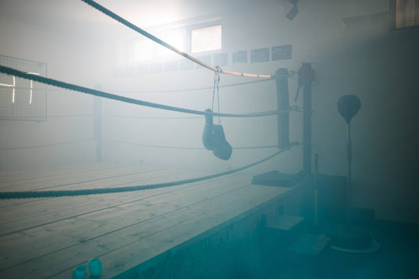 Boxing gloves hanging on a rope on empty boxing ring for training in dark gym.