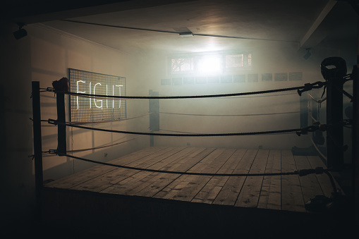 Empty boxing ring for training in dark gym. Neon fight sign is on the wall by the ring.