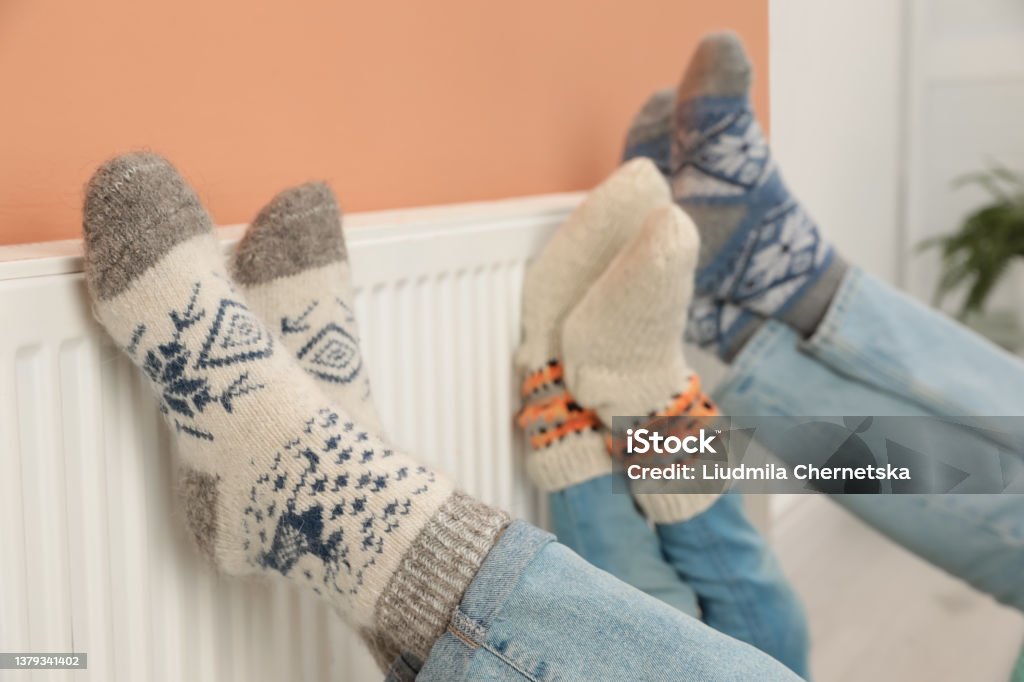 Family warming legs on heating radiator near color wall, closeup Radiator - Heater Stock Photo