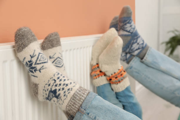 Family warming legs on heating radiator near color wall, closeup Family warming legs on heating radiator near color wall, closeup heat home interior comfortable human foot stock pictures, royalty-free photos & images